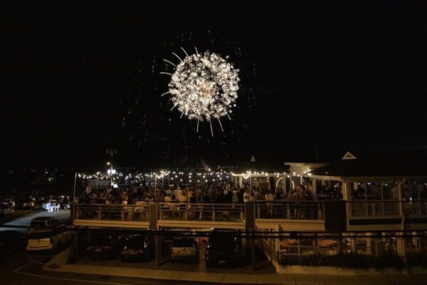 a crowd gathered outside a venue, watching a spectacular firework display in the night sky.