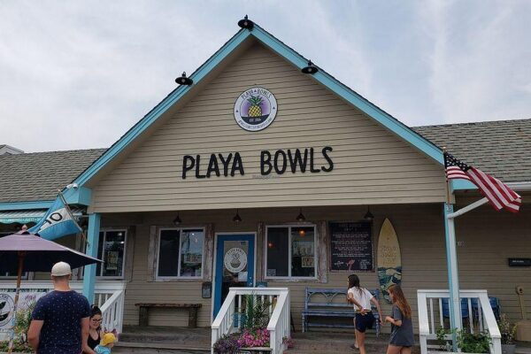 exterior of Playa Bowls, a beach-themed eatery with a light brown building and and peple walking in and out of the restaurant